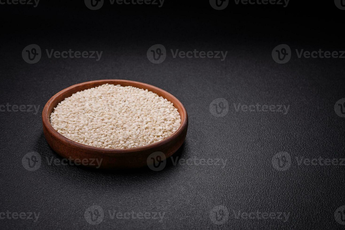 White uncooked rice in a round ceramic bowl on a dark concrete background photo