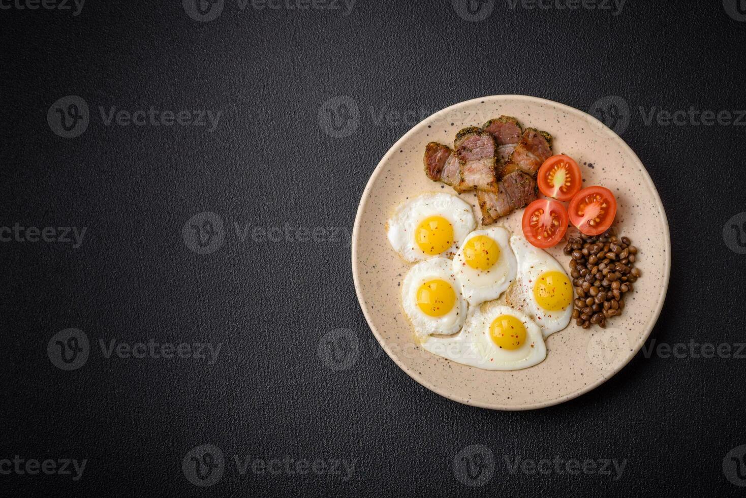 Delicious nutritious breakfast of fried quail eggs, bacon, legumes and cherry tomatoes photo