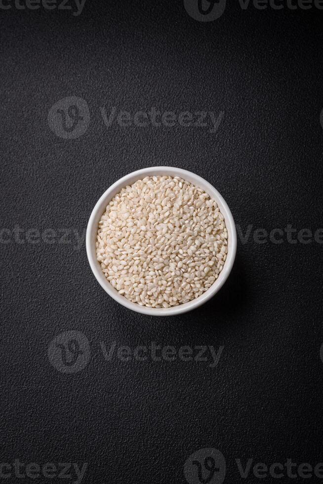 White uncooked rice in a round ceramic bowl on a dark concrete background photo