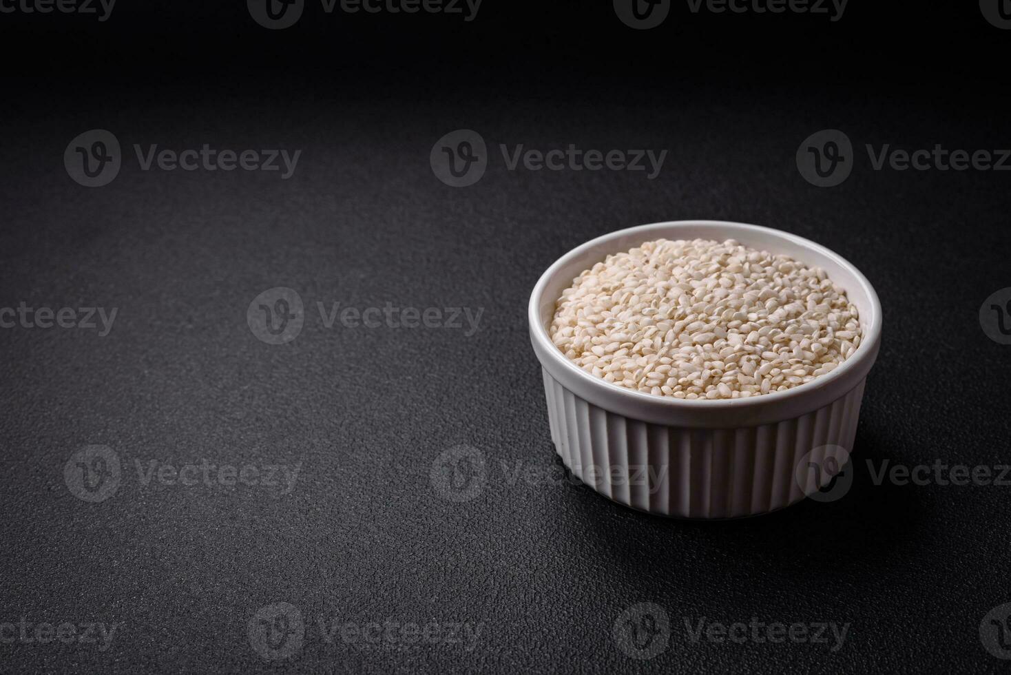 White uncooked rice in a round ceramic bowl on a dark concrete background photo