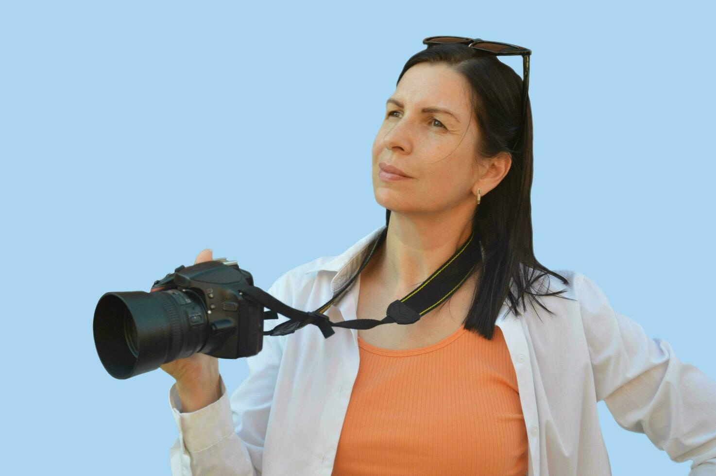 retrato de un joven mujer - fotógrafo, en un blanco camisa, en pie con un cámara y mirando dentro el distancia, aislado en un azul antecedentes. gratis espacio para proceso de copiar. foto