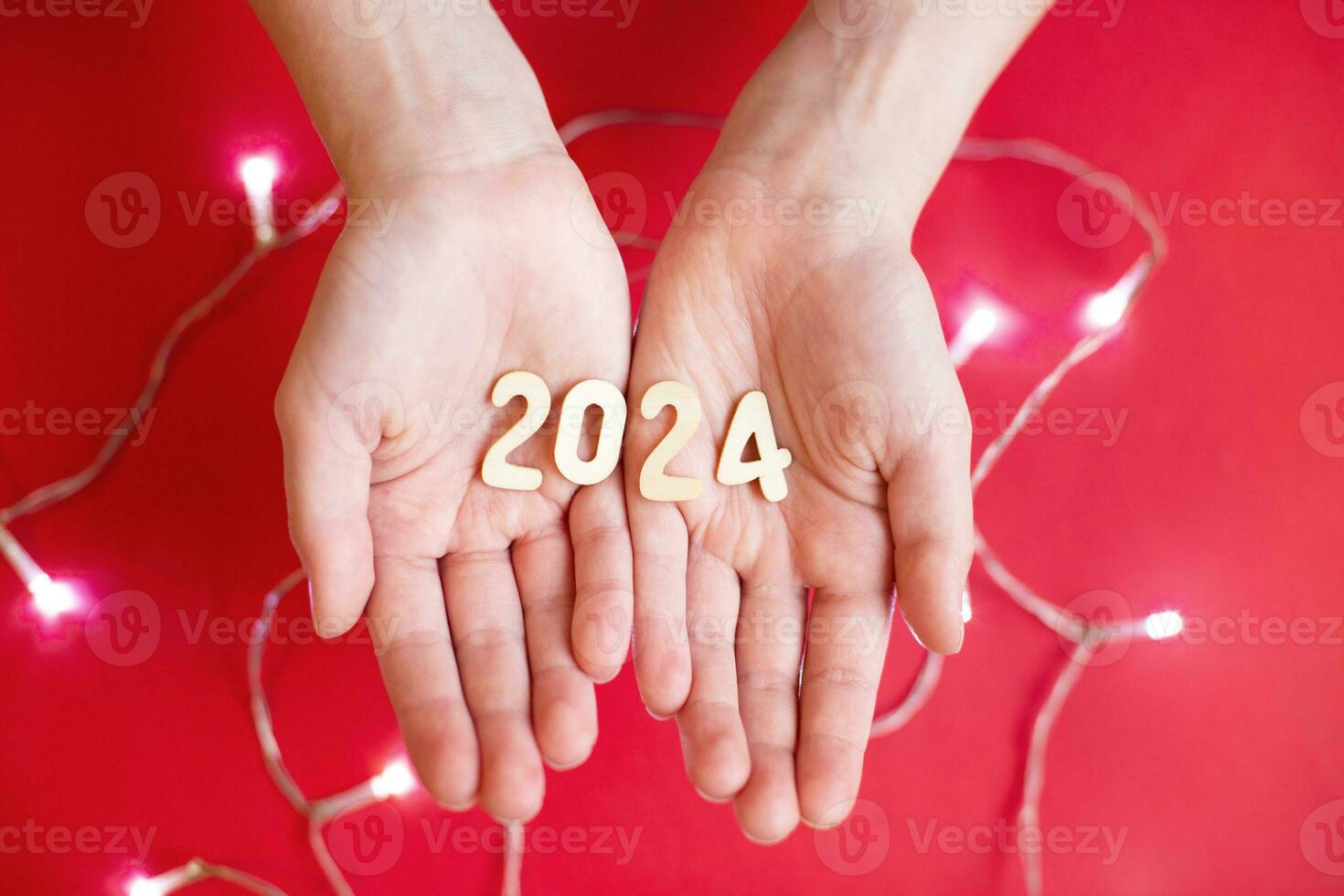 Child hands holding wooden number 2024 on palms on festive red background with copy space photo