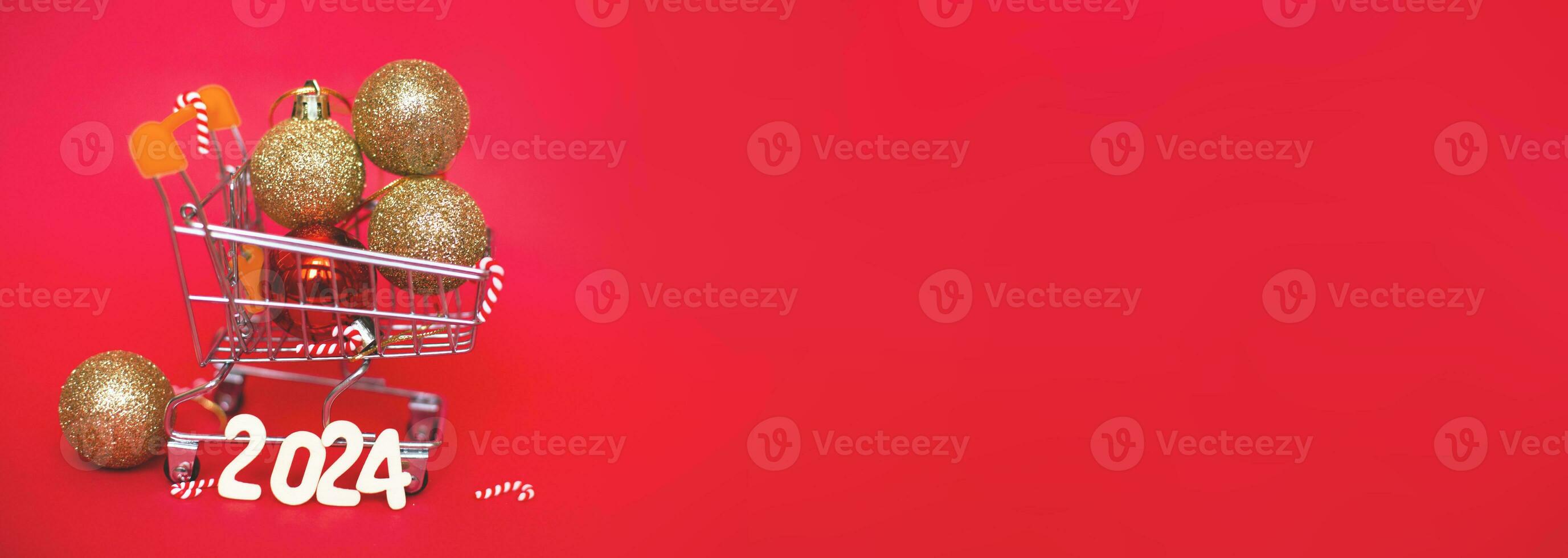 Christmas balls in shopping cart with garland and wooden numbers 2024 on red background. photo