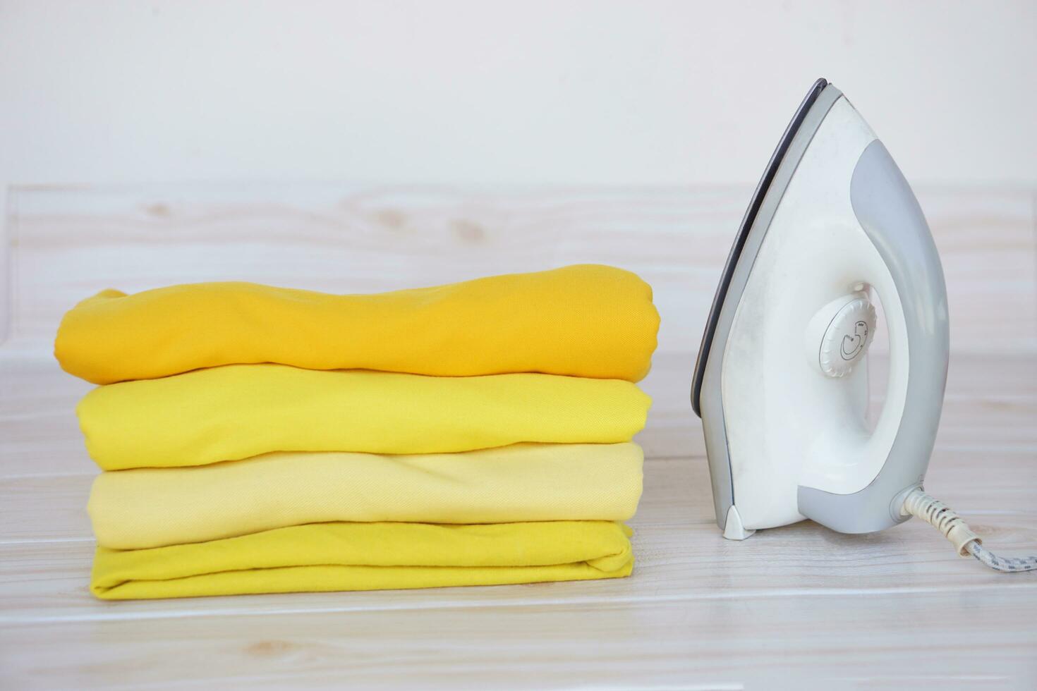Stack of folded yellow clothes and electric iron on table. Concept, daily chore, household. ironing and folded clothes for neat and clean. Maintenance and keep garments. photo