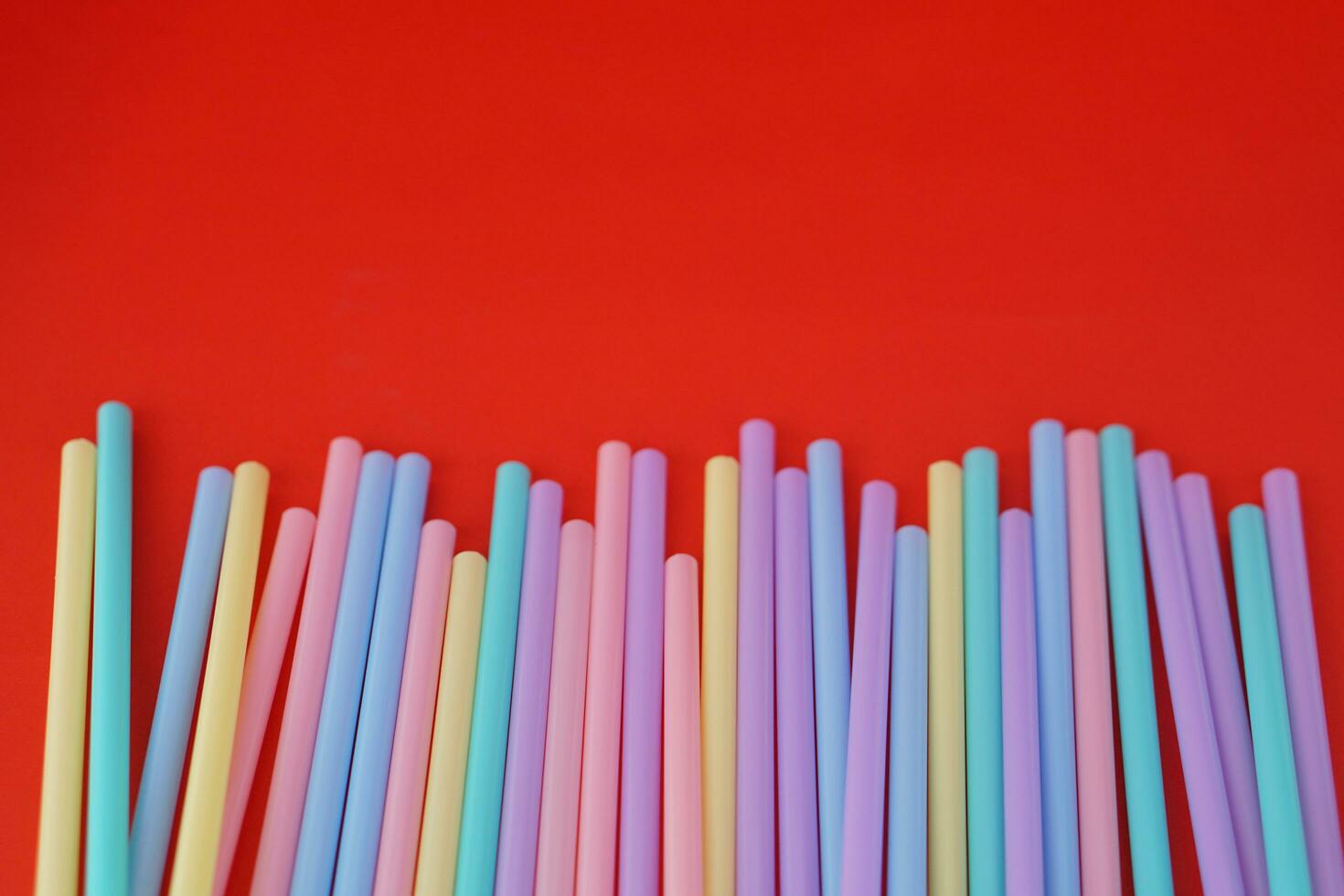 Colorful plastic drinking straws tubes for juice and cocktails, red background. Concept, single use equipment for drinking, but can use for diy crafts for decoration. photo