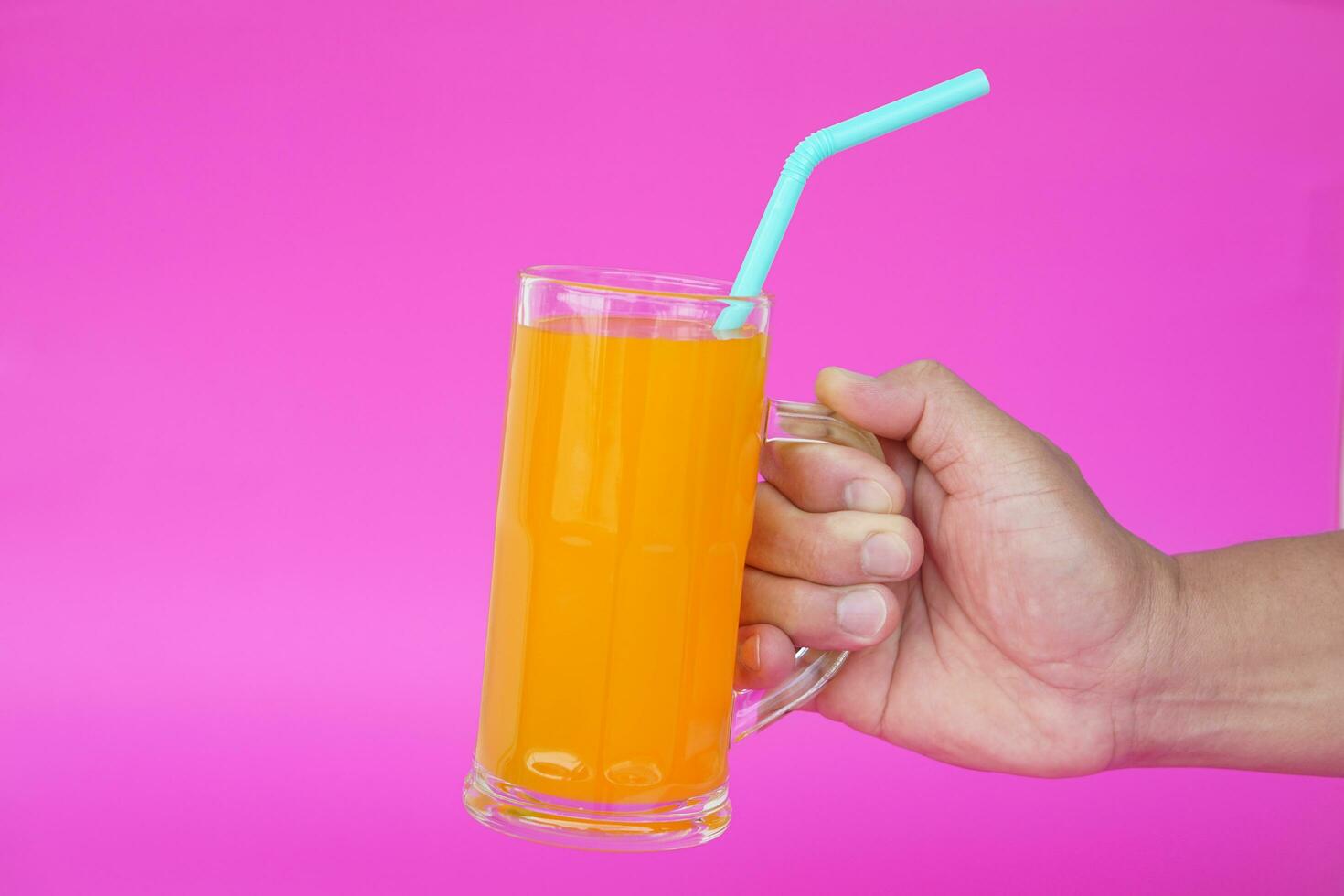Close up of man hand holding glass of orange juice with drinking straw, on pink background. Concept, morning refreshing beverage. Sweet, testy and high vitamin C. photo