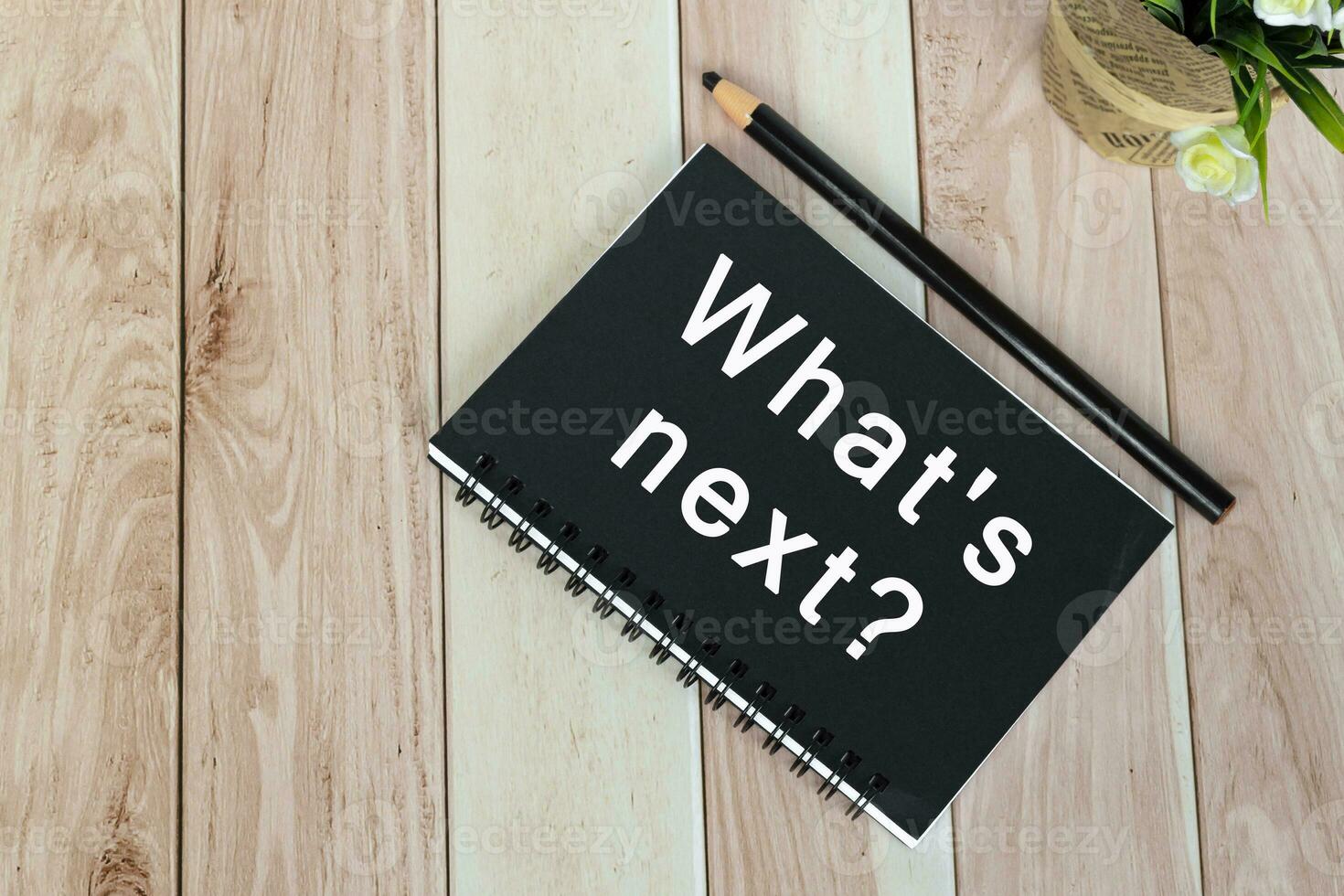 What's next text on notepad on wooden desk with potted plant. photo