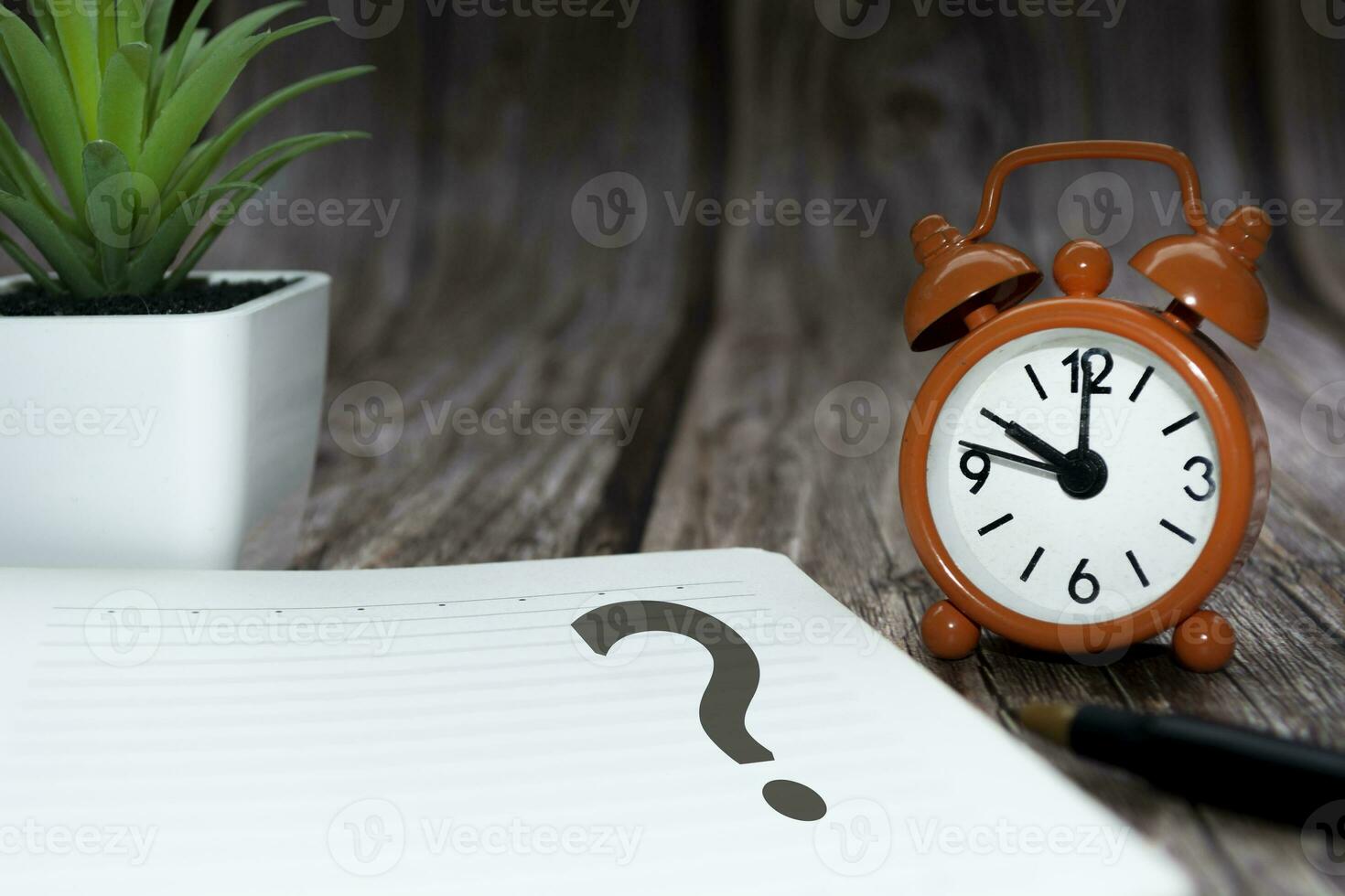 Question mark on notepad alarm clock set at 10 oclock on wooden background. photo