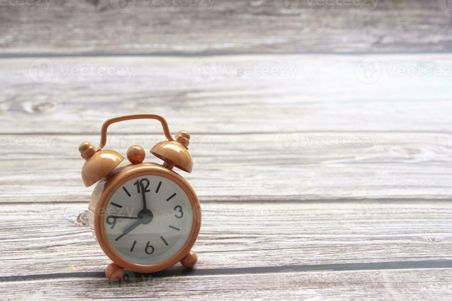 Orange alarm clock isolated on wooden desk. The clock set at 8 o'clock. photo