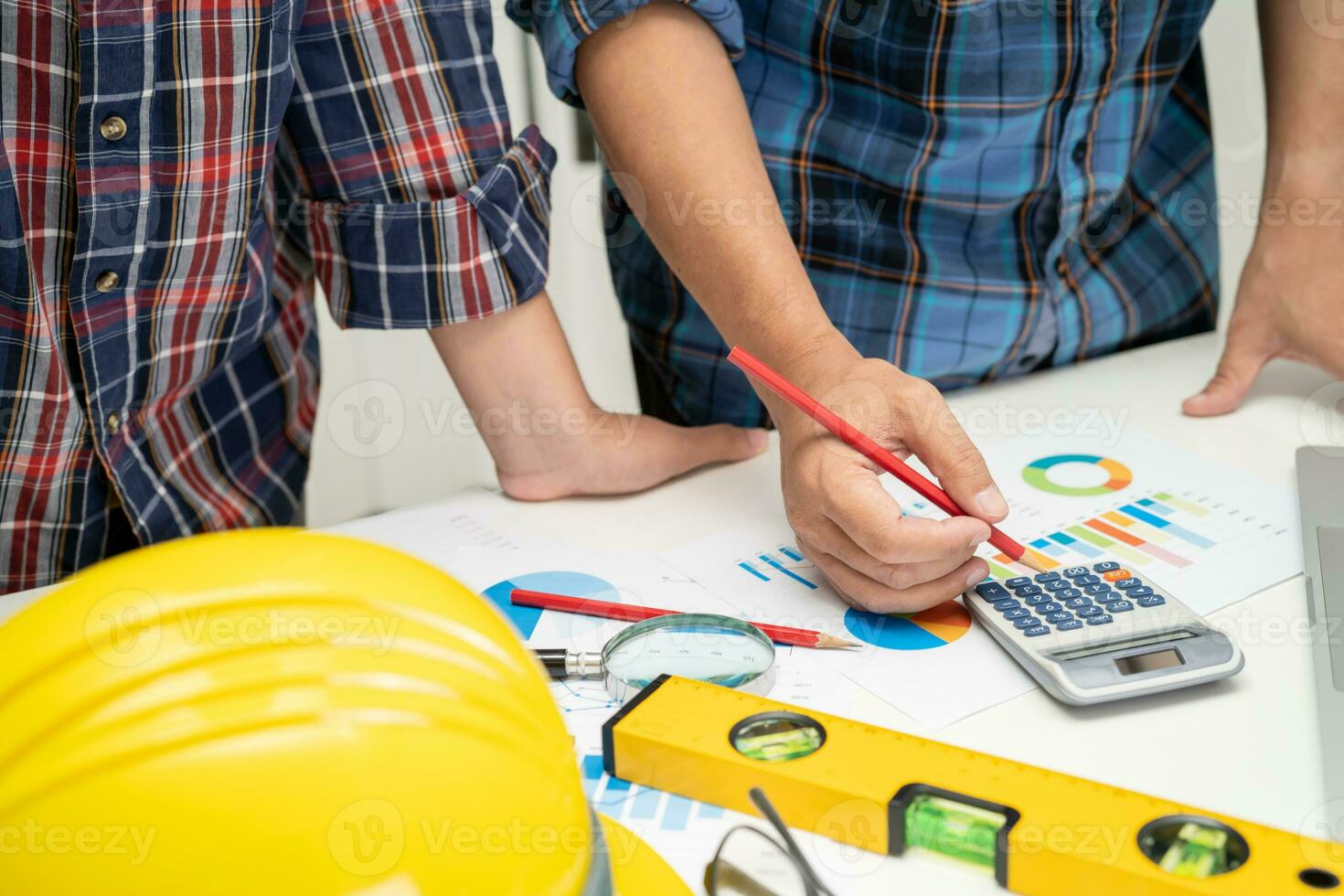 Asian engineer and partner team learn and talk with house plan project blueprint, graph and yellow helmet and engineering construction tools on table work. photo