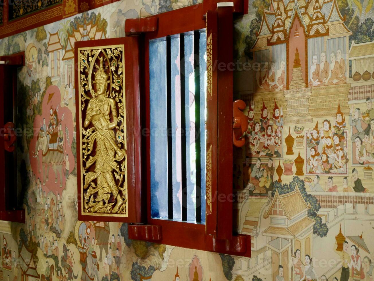The wooden window is carved in the image of an angel holding a flag. at Wat Phra Singh Chiang Rai, Beautifully Carved Red and Golden Door at the Wat Phra Singh Temple in Chiang Rai, Thailand photo