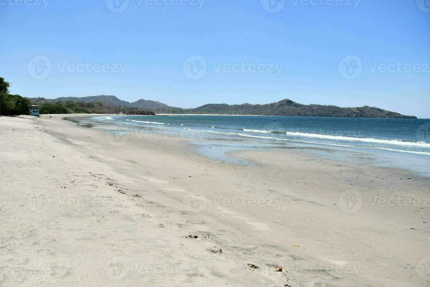 a sandy beach with a blue sky and mountains in the distance photo