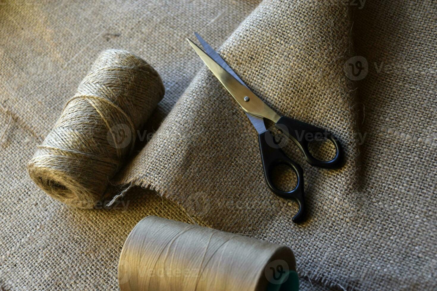 Yellow skeins of thread and scissors on a background of burlap. Yellow coarse cloth threads and scissors. photo