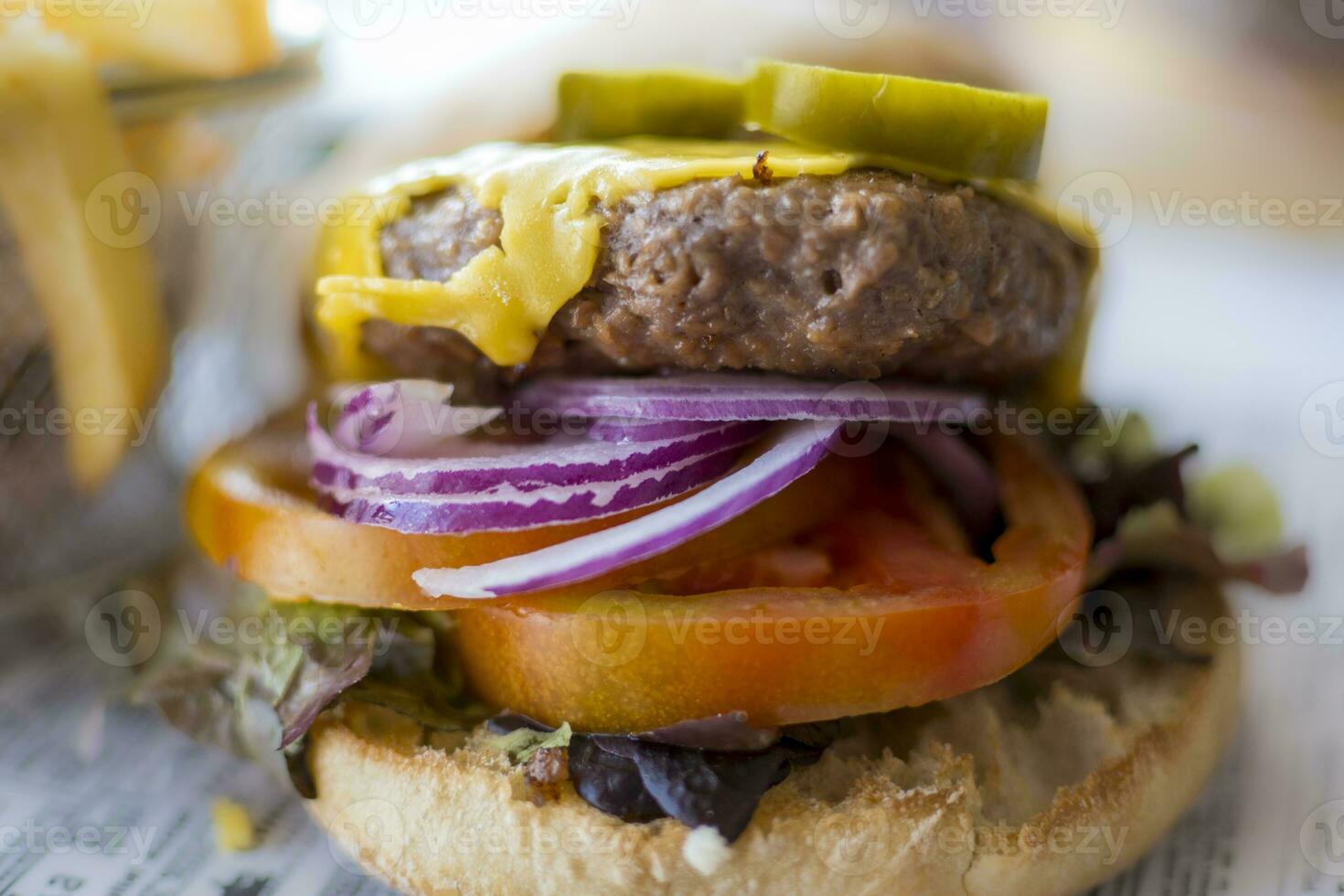 Selective focus close-up shot of a vegan burger bun with plant-based cheese, onion and tomato photo