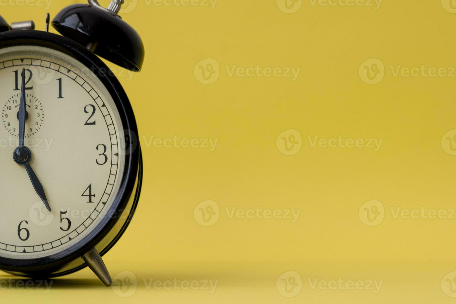 Analog alarm clock displaying five o'clock on a yellow background with copy space photo