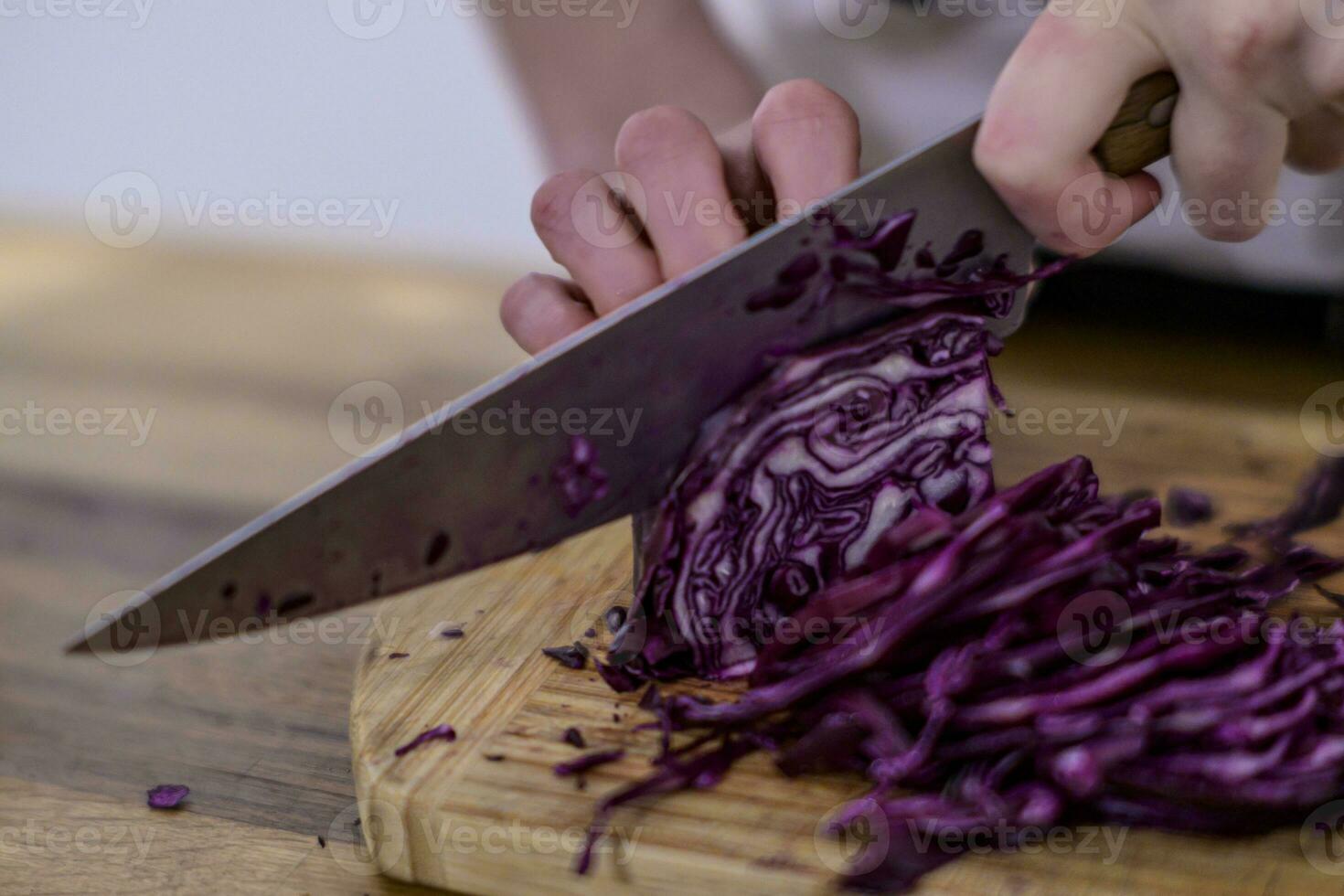 chopping red cabbage with a kitchen knife on a wooden cutting board photo
