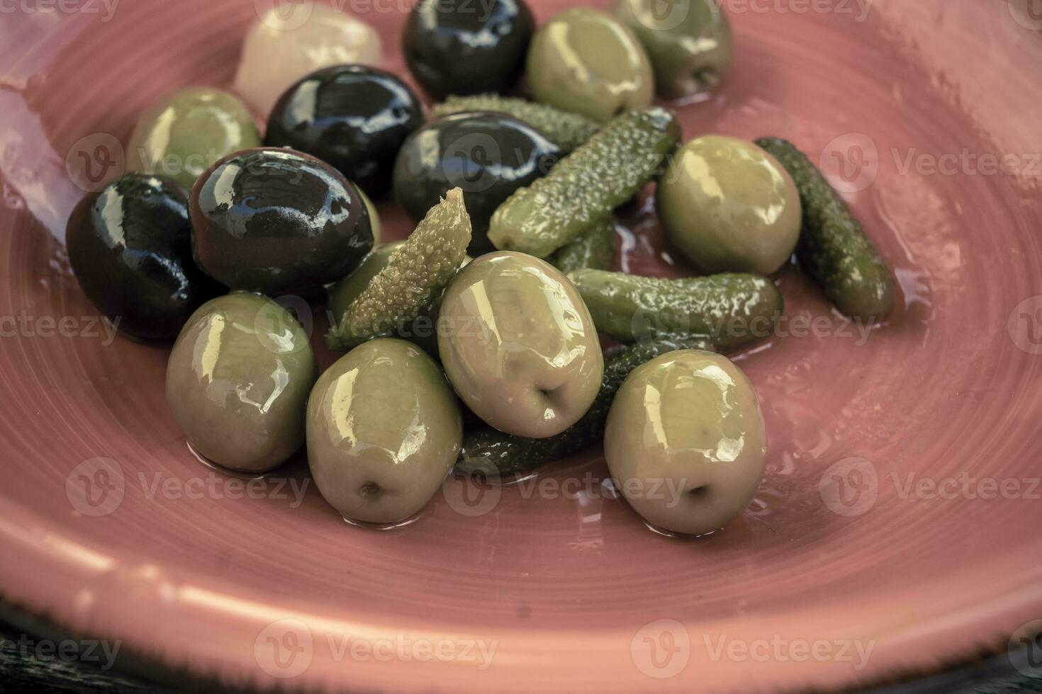 Close-up shot of mix of black and green olives with pickle in an orange bowl. photo