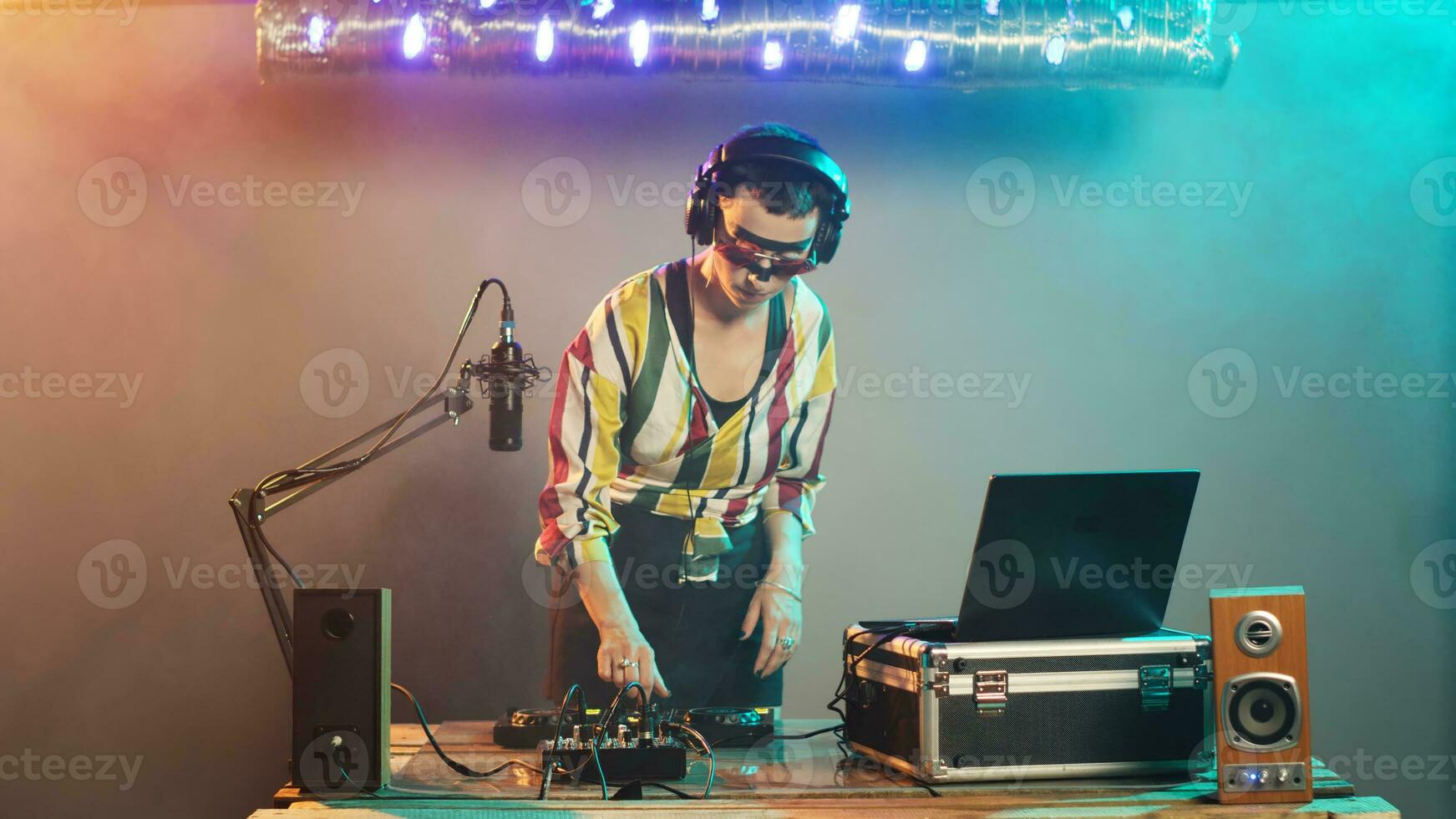 DJ performer creating techno music at control buttons, wearing crazy makeup and mixing at audio stereo equipment. Artist playing disco sounds at turntables for nightclub party event. Tripod shot. photo