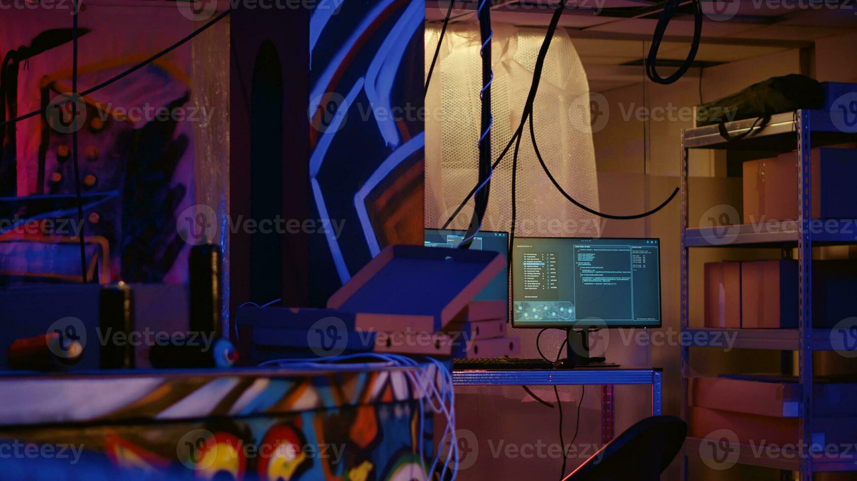 Zoom in on advanced technology computers left open running code in empty neon lit basement with graffiti drawings painted on walls. High tech equipment used by hackers in underground warehouse photo
