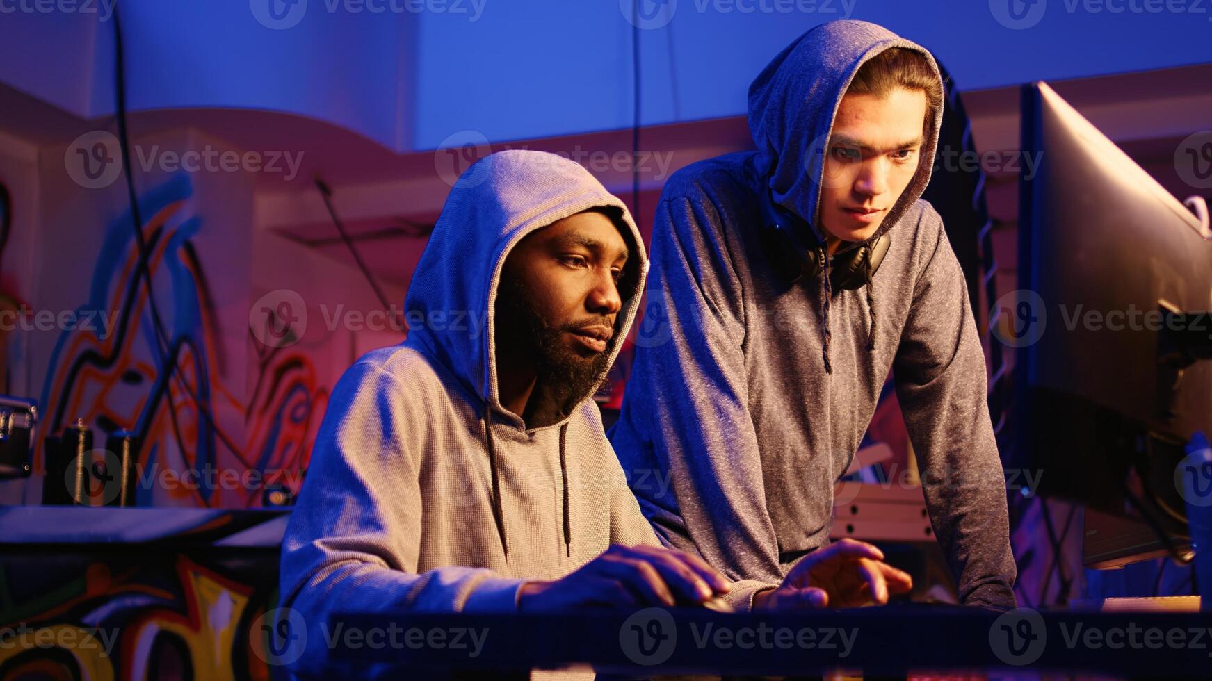 African american hacker talking to asian colleague in rundown hiding place, brainstorming ways to find exploits for system vulnerabilities and use them to ask system owner for ransom photo