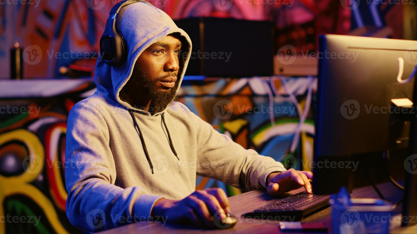 Hacker stealing credit card numbers and manipulating banking systems for his own personal gain while listening to music through headphones. Evil developer programming in graffiti painted basement photo