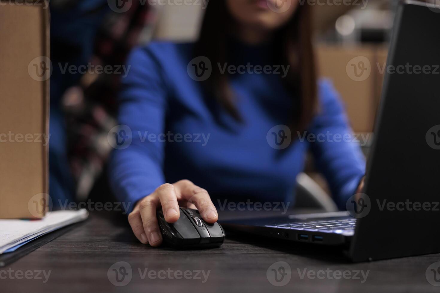Woman managing parcel delivery on laptop in retail ecommerce warehouse. Logistics manager doing inventory check on laptop while using computer mouse with close up on hand photo