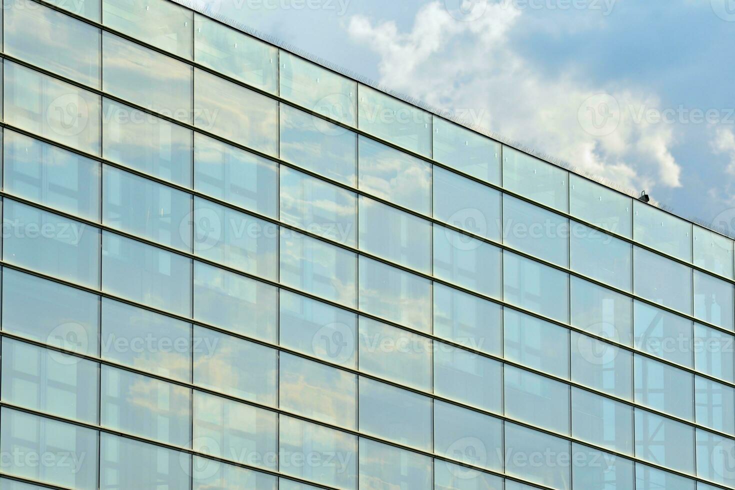 Glass building with transparent facade of the building and blue sky. Structural glass wall reflecting blue sky. Abstract modern architecture fragment. Contemporary architectural background. photo