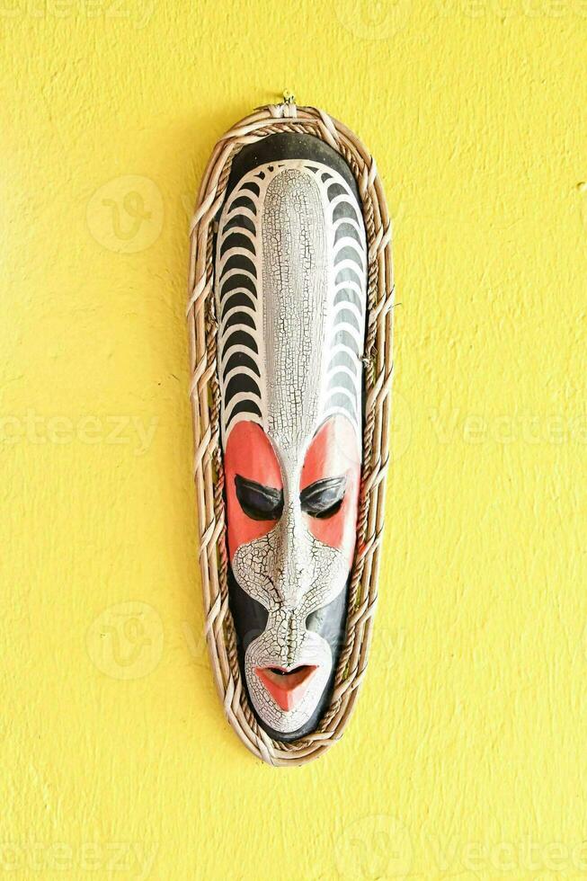 a wooden mask hanging on a yellow wall photo