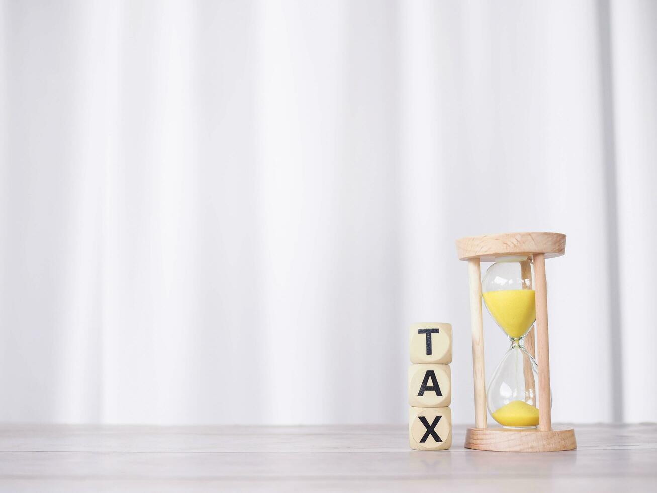 Hourglass and wooden blocks with the word TAX on stack of coins. The concept for manage time to paying tax photo