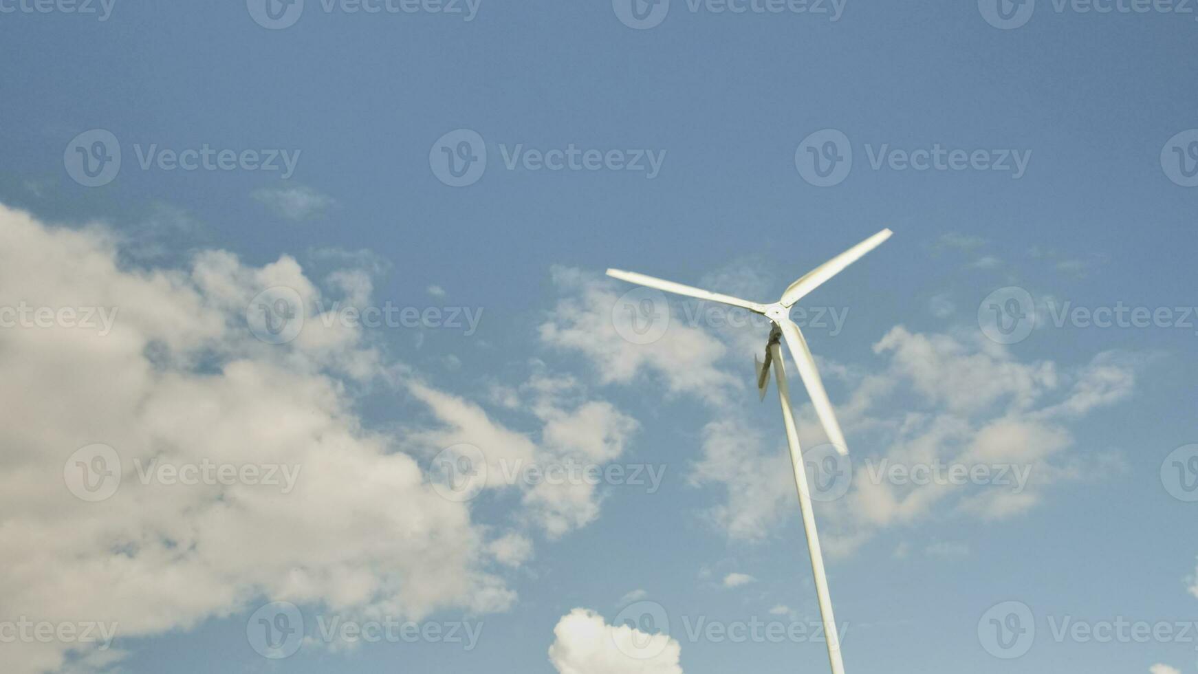 One white windmill in blue sky and clouds background, turn in wind to generate clean electric energy industry, natural power resource technology for sustainable ecology and environment conservation. photo