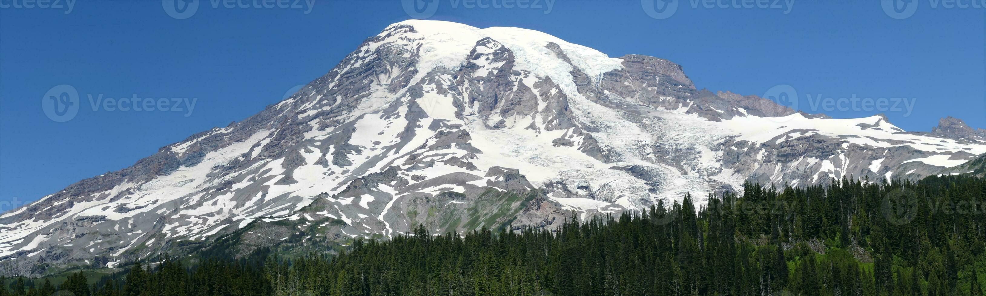 Summit of Mt Rainier rises above conifer forested hills photo
