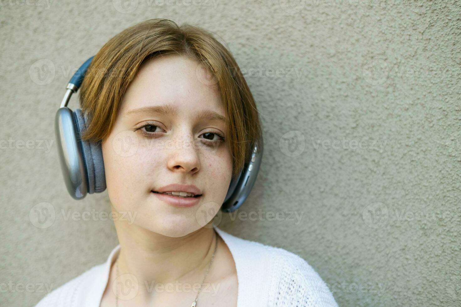 Portrait of a teenage girl in headphones against a gray wall. photo