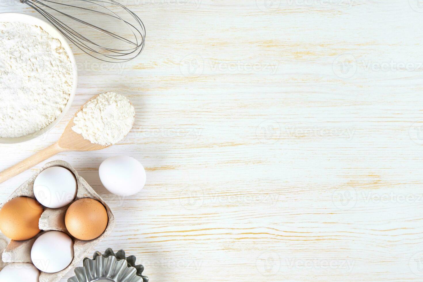 Baking ingredients flour, eggs, milk, bakeware on white wooden background with copy space photo