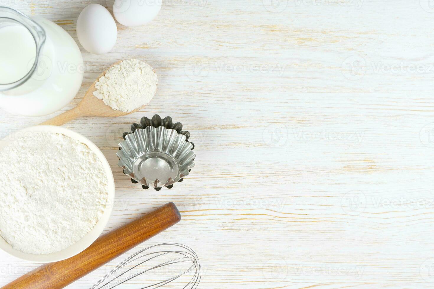Baking ingredients flour, eggs, milk, bakeware on white wooden background with copy space photo