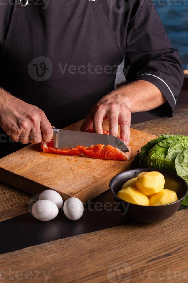 de cerca de vestido en negro cocinero cortes con cuchillo el salmón a el profesional cocina. foto