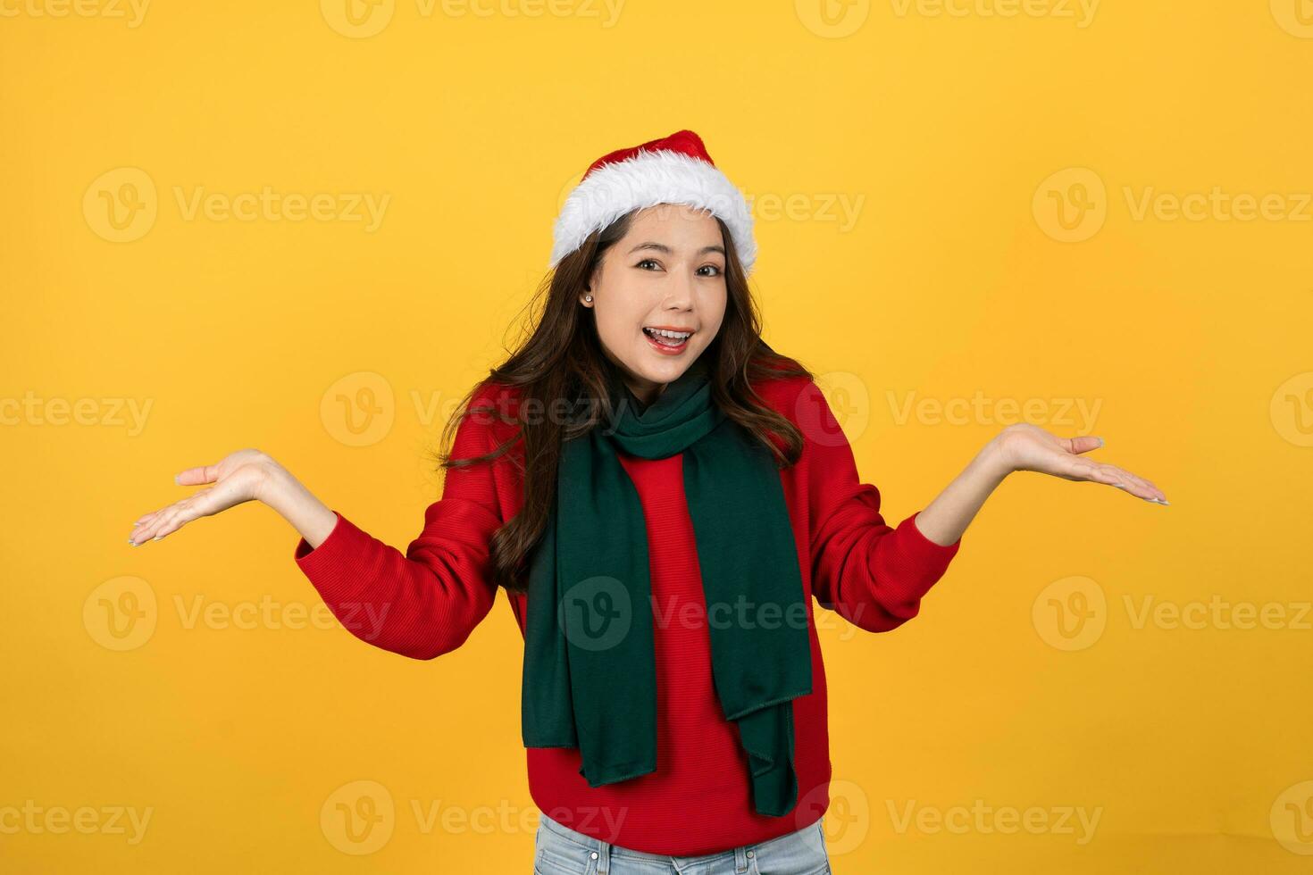 Beautiful happy excited Asian woman wearing a Christmas sweater. She is making two open palm gestures isolated on yellow studio background. photo