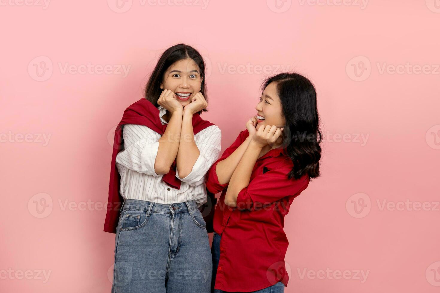 dos asiático niña amigos en blanco y rojo camisas sonrisa, actitud con abierto bocas y Mira sorprendido en rosado aislado antecedentes. foto