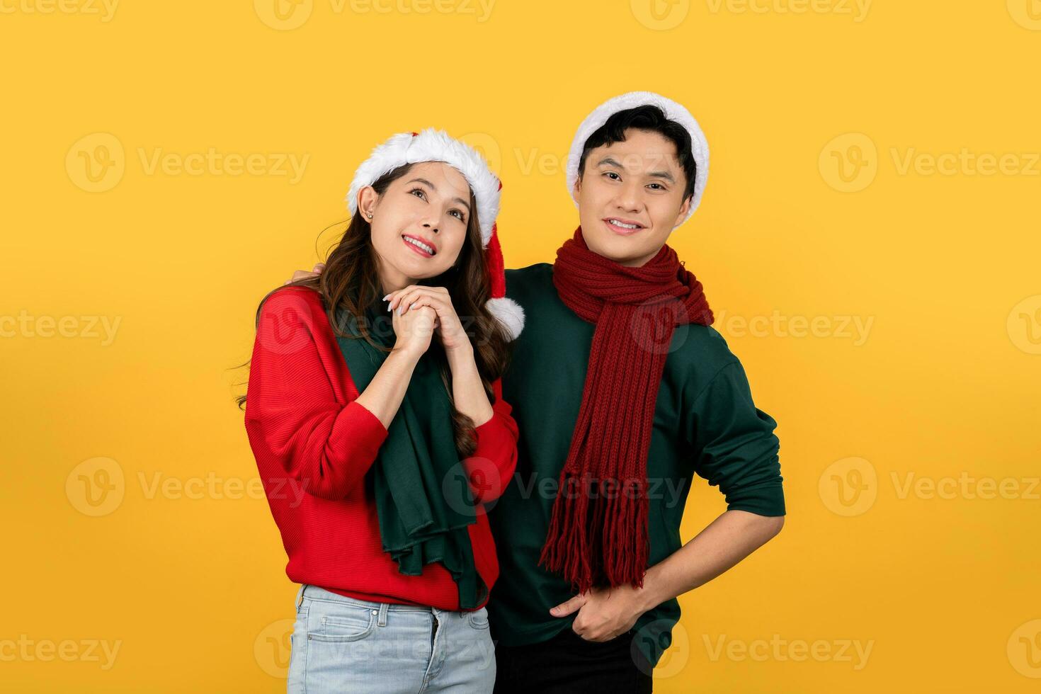 Asian couple wearing Christmas sweaters and hats in yellow background studio photo