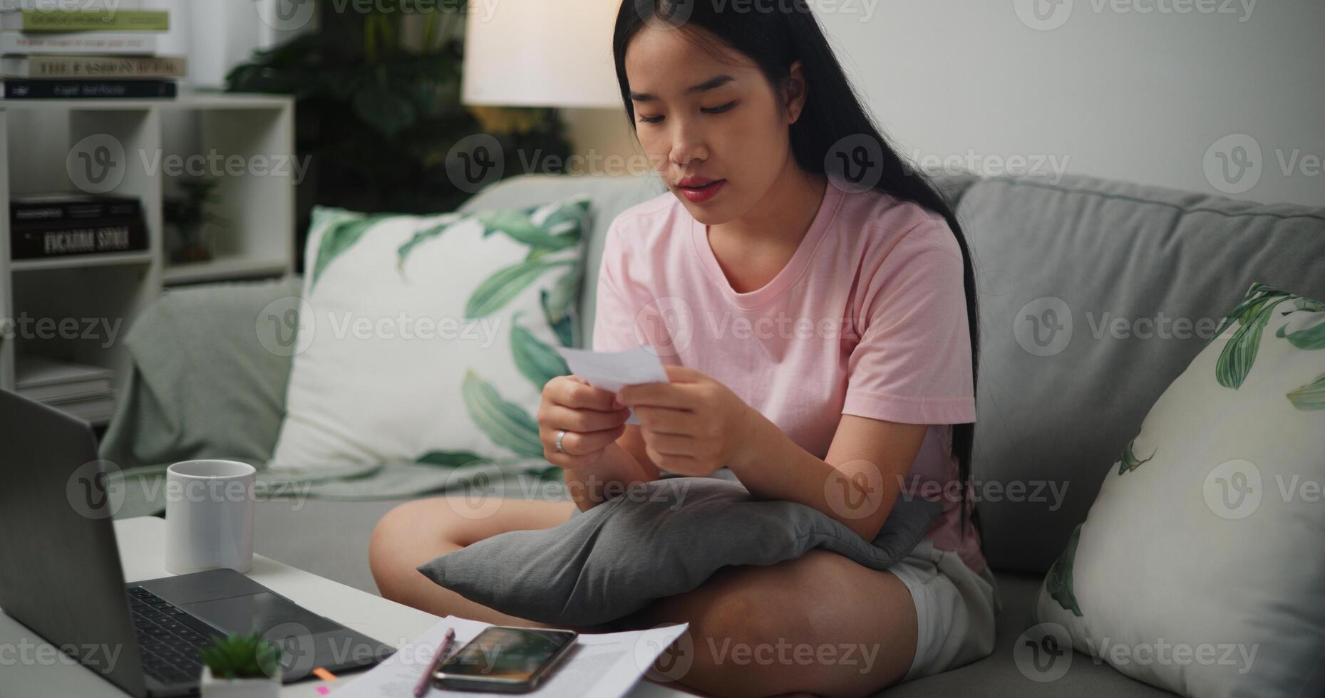 Portrait of Young Asian woman holding paper various expense bills and plans for personal finances and using calculator on smartphone calculate Income and expenses at home,Home finance photo