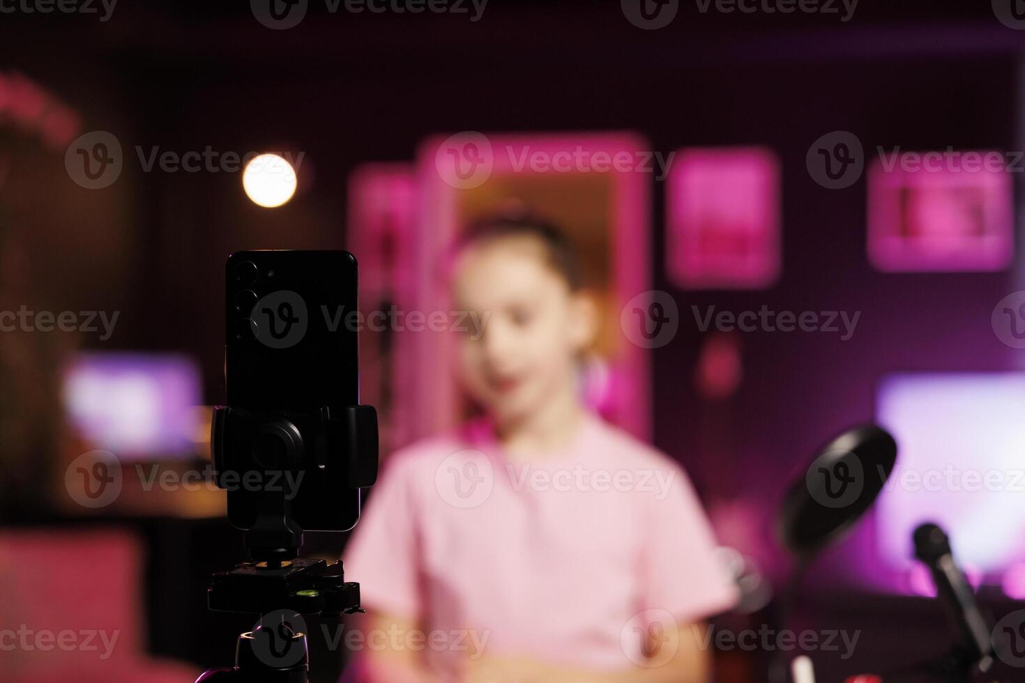 Close up shot of professional recording cellphone camera used by young internet star to do livestream. Focus on video production gear used by child in blurry background to do live broadcast photo