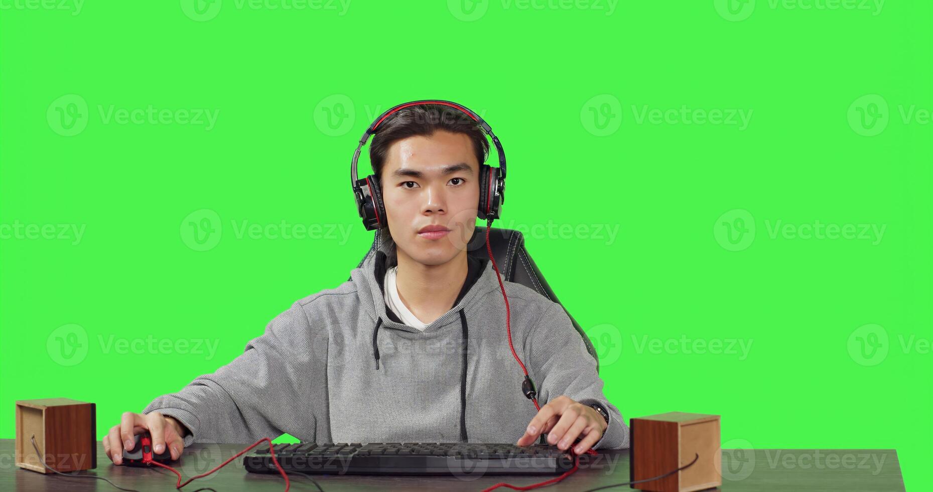 POV of asian man plays pc videogames at desk, sitting against greenscreen background. Gamer having fun with friends online on gaming contest, wearing headphones at workstation. photo
