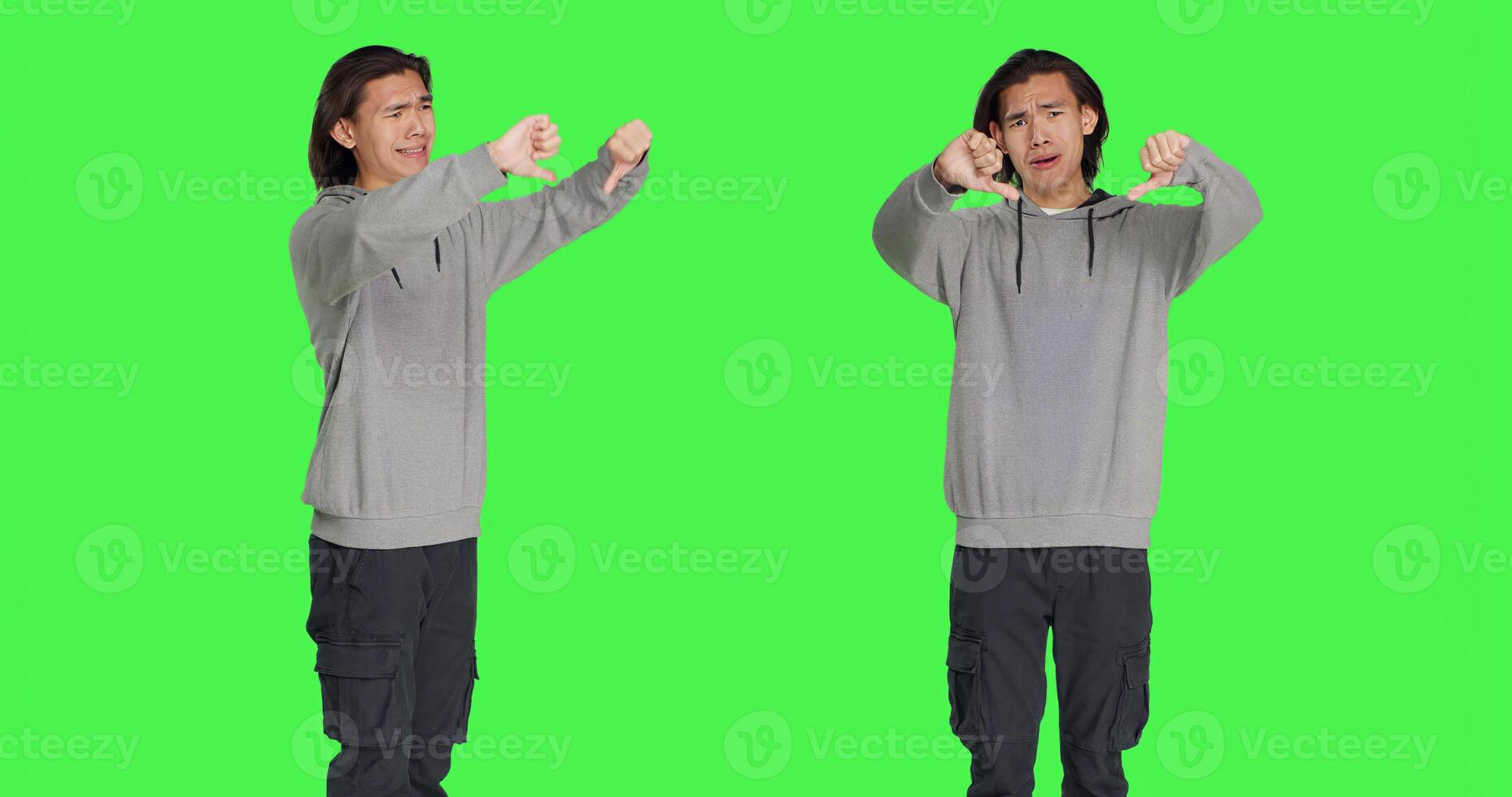 Asian person shows thumbs down sign and feeling disappointed in front of isolated greenscreen background, negative facial expressions. Man does dislike symbol and expressing disapproval. photo