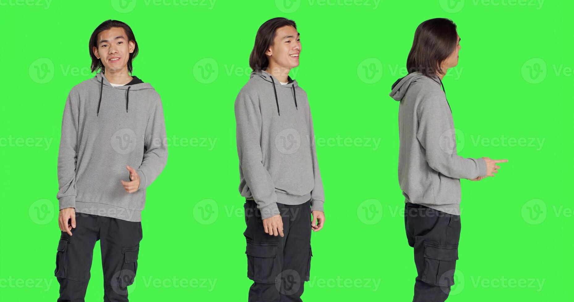 Asian person shows approval sign over greenscreen backdrop, doing yes gesture and smiling. Young man with optimistic facial expressions feeling pleased and expressing agreement. photo