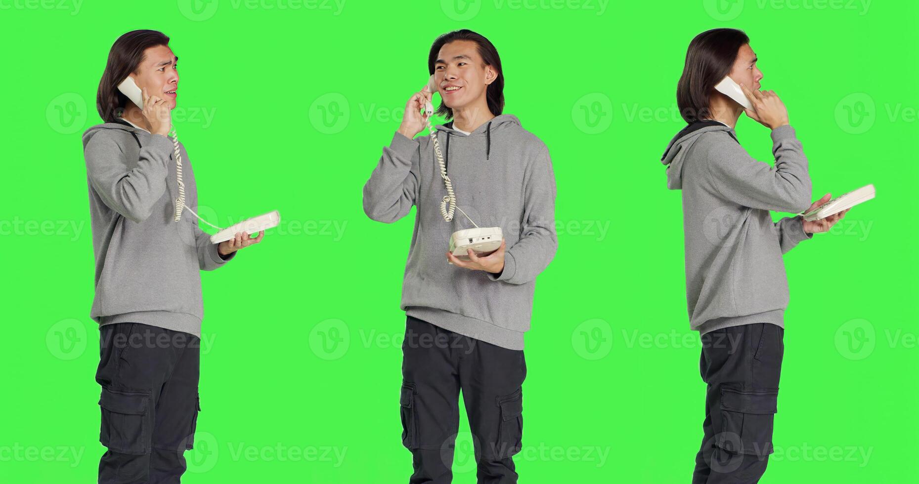 Asian person talking on landline phone, answering call on telephone with cord while he stands against greenscreen backdrop. Young adult using retro phone for remote communication. photo