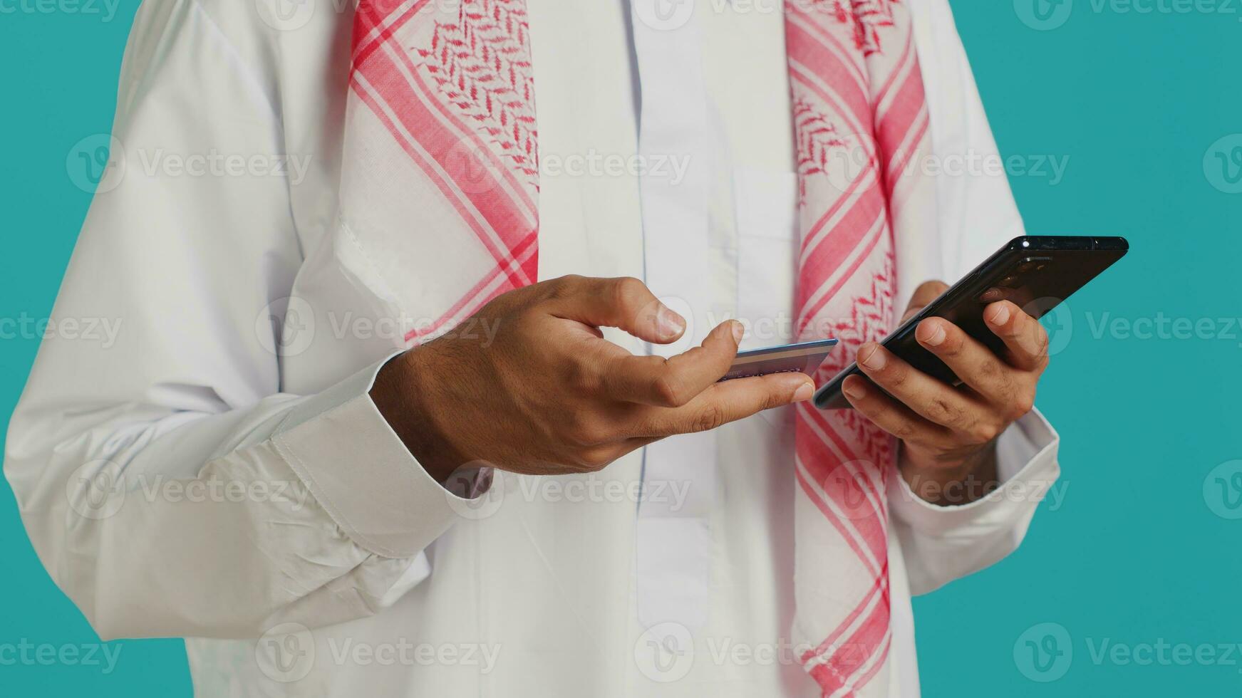 Muslim man adding card information on webpage, doing online shopping session while he wears traditional islamic attire with headscarf. Person paying for objects on web store, banking service photo