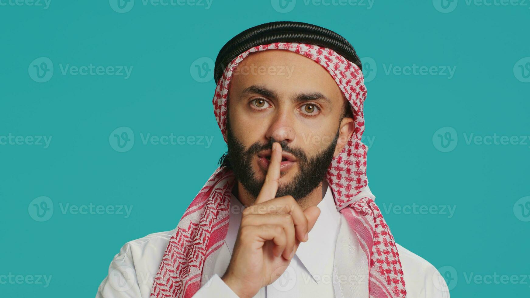 On camera, arabic person makes quiet signal with finger over lips, displaying silent mute gesture. In studio, private person does secretive confidentiality sign in an effort keep secret. photo