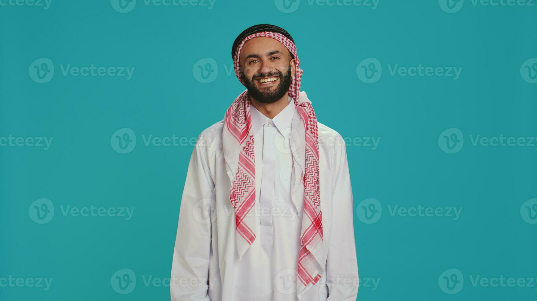 Muslim guy nodding in studio shot, saying yes and expressing his approval. Arab person in traditional clothes showing support about something. Middle eastern man doing positivity and agreement sign. photo