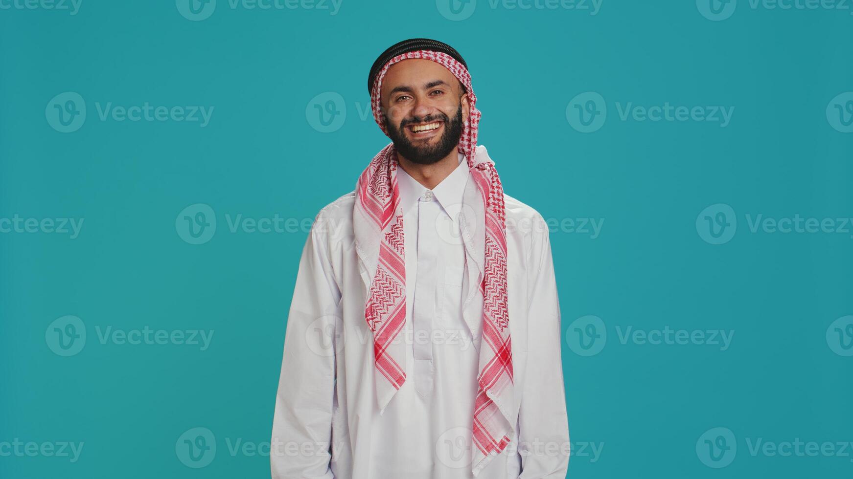 Muslim guy nodding in studio shot, saying yes and expressing his approval. Arab person in traditional clothes showing support about something. Middle eastern man doing positivity and agreement sign. photo