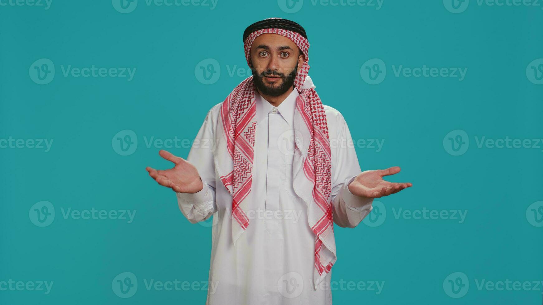 Islamic adult acting unsure and clueless in studio, showcasing i dont know sign and being confused over blue background. Young person in arab clothing feeling uncertain and shrugging. photo