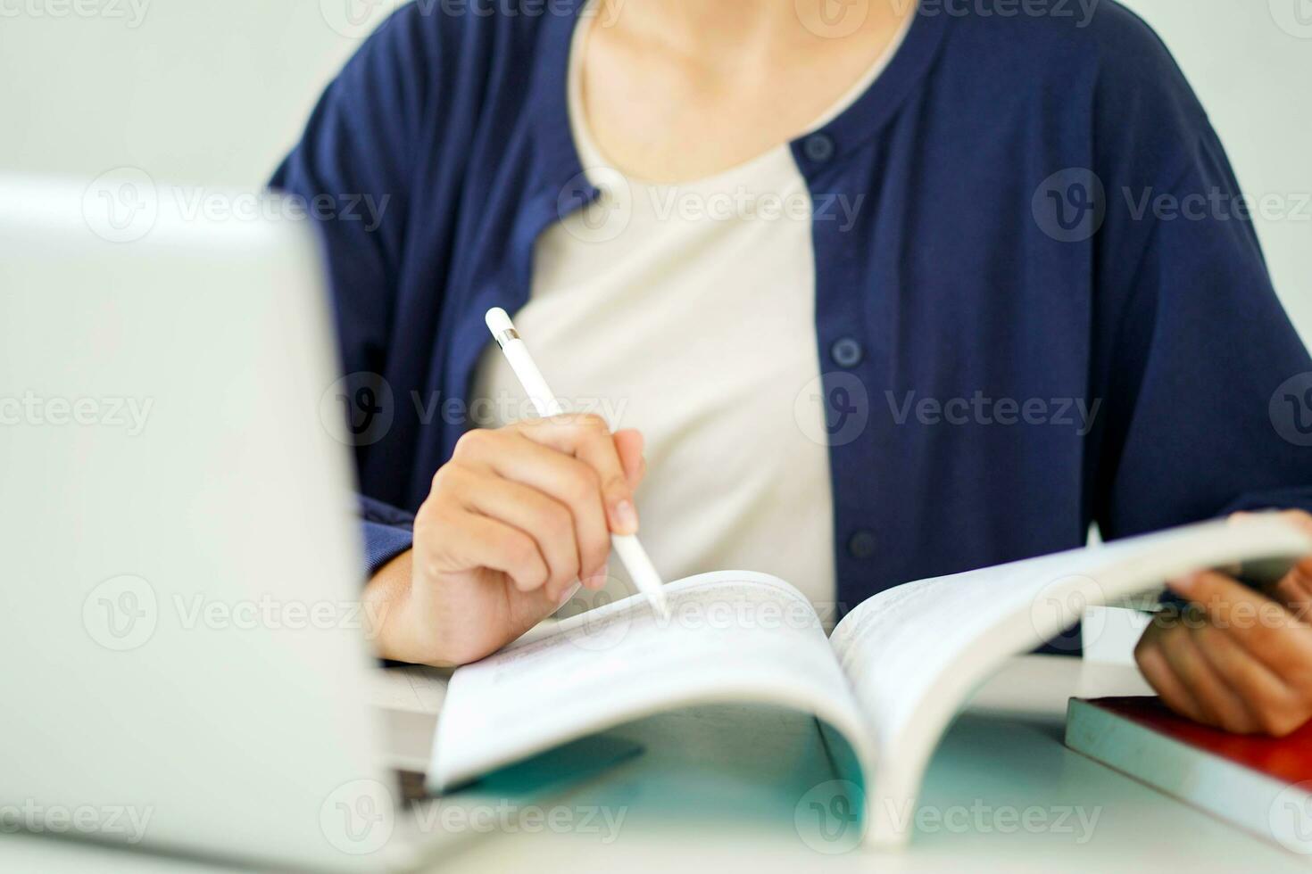 Closeup and crop young female student in casual cloth reading a book with laptop for the exam on blurred background. photo